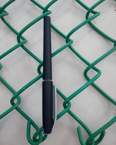 Ein schwarzer Stift wird auf grünes PVC beschichtete Kettengliedzaun gesetzt und die Länge zwei Löcher ist mit der Länge eines Stiftes gleichwertig.